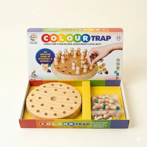 Studio shot of the "COLOUR TRAP" board game unboxed on a clean, light cream background. The colorful retail box stands open in the background, showing a hand playing the game on its cover. In the foreground, the box insert neatly holds the circular wooden game board with peg holes on the left, and a transparent plastic zip pouch filled with wooden pegs with colorful bases on the right.