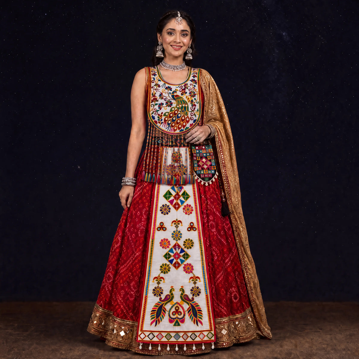 A woman modeling a heavily embroidered red and white traditional Indian outfit with a gold dupatta, set against a dark starry background.