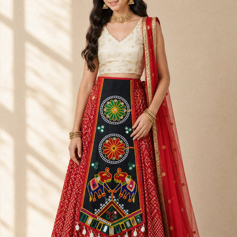 Black | A woman models a traditional Indian ethnic outfit consisting of a red patterned skirt, a cream-colored embroidered blouse, and a red dupatta with gold borders, set against a warm beige background with soft window shadow patterns.