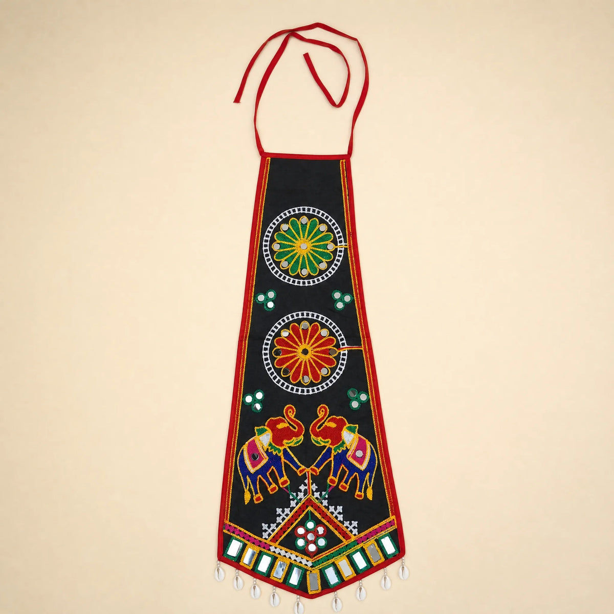 Black | A traditional Indian black cotton apron with red neck and waist ties, decorated with colorful hand-embroidered motifs including elephants, floral patterns, and geometric designs, set against a solid beige background.