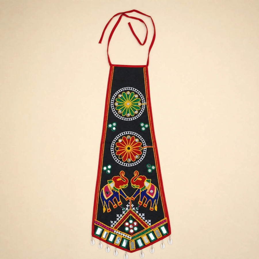 Black | A traditional Indian black cotton apron with red neck and waist ties, decorated with colorful hand-embroidered motifs including elephants, floral patterns, and geometric designs, set against a solid beige background.