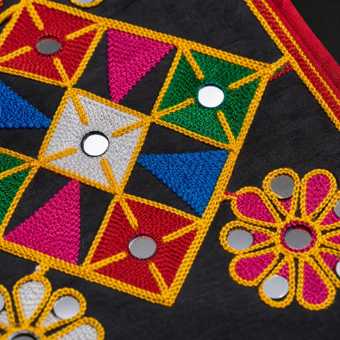 Black | Close-up of a black embroidered textile with geometric and floral patterns in bright pink, red, green, blue, yellow, and white, accented with small round silver mirror embellishments.
