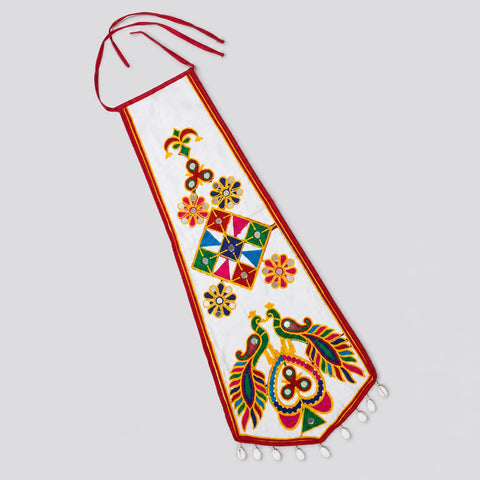 White | A white fabric wall hanging or decorative banner with red trim, colorful folk-art style motifs including flowers, a central geometric diamond pattern, and peacocks, shown on a light gray background.