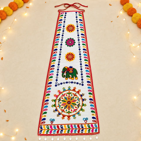 White | A white fabric wall hanging or decorative banner with colorful embroidered patterns, including an elephant motif and floral motifs, displayed flat on a light beige background with decorative string lights and pom-poms around the edges.