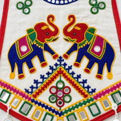 White | Close-up of a white embroidered textile featuring two large blue elephants facing each other, with red trunks and ornate pink, green, yellow, and blue decorative motifs. Mirrored square embellishments and red border trim are visible.