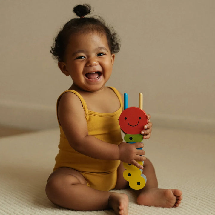 Toddler laughing with a wooden pull-along caterpillar toy