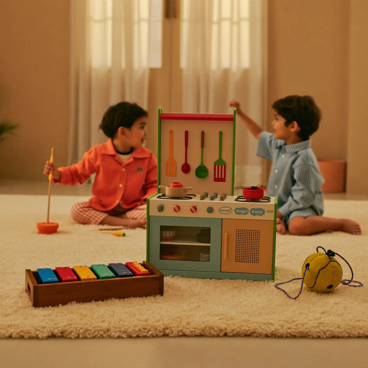 Two children playing with a toy kitchen set and xylophone